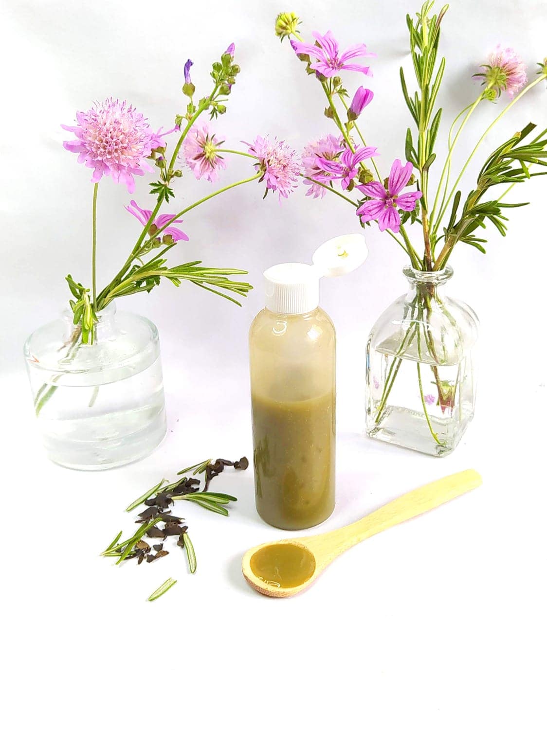 Crear extractos vegetales efectivos para tus fórmulas cosméticas 16 Gel natural con extractos vegetales en botella, con flores de malva, romero y una cuchara de madera